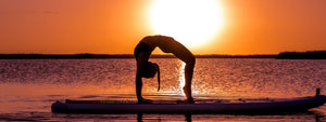 Yoga upward bow wheel pose on a paddle board at sunset