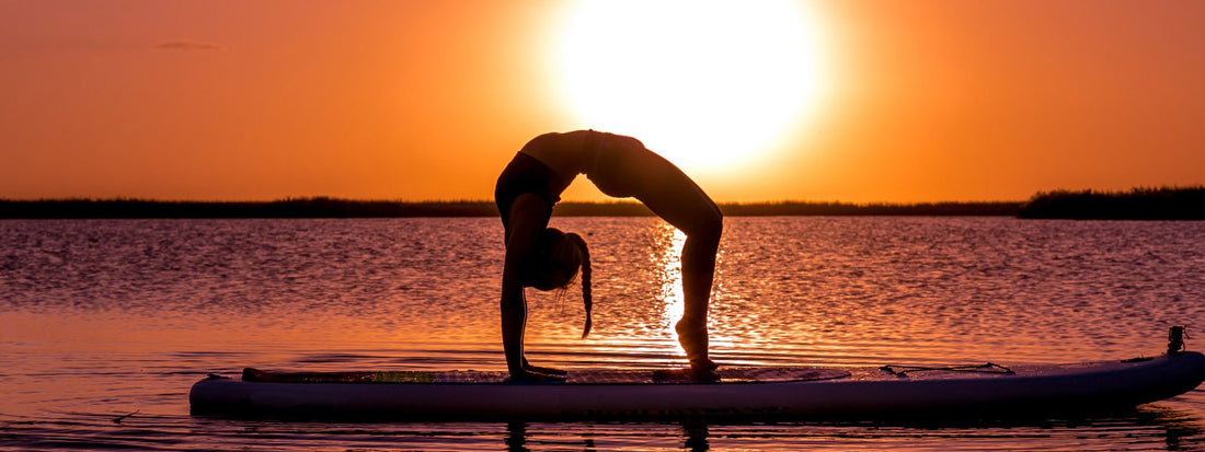 Yoga upward bow wheel pose on a paddle board at sunset